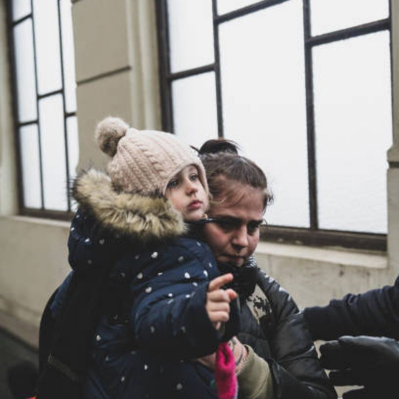 Lviv, Ukraine - March 5, 2022: Inside the Lviv train station, someone reaches out a helping hand toward a woman carrying a child up the steps to as they walk toward a Poland-bound train.